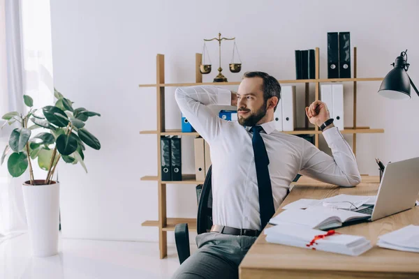 Avvocato che si allunga mentre è seduto sul posto di lavoro con computer portatile in ufficio — Foto stock