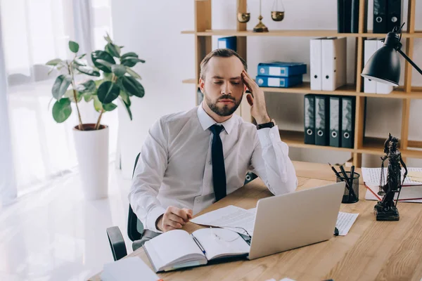 Портрет втомленого адвоката, який сидить на робочому місці з ноутбуком і документами в офісі — стокове фото