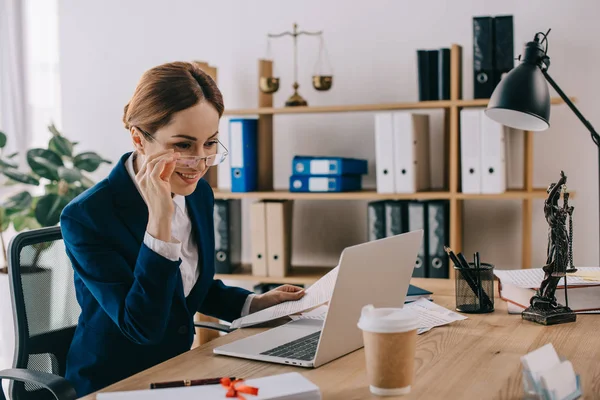 Avvocato sorridente femminile che guarda lo schermo del computer portatile sul posto di lavoro in ufficio — Foto stock