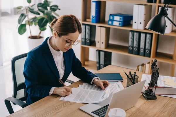 Vue latérale de avocate faisant de la paperasserie sur le lieu de travail avec ordinateur portable au bureau — Photo de stock