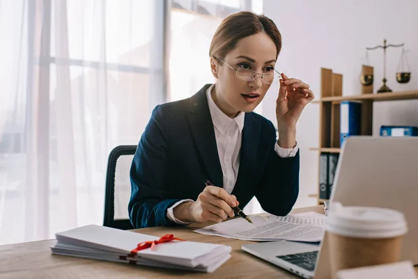 Visão lateral do advogado feminino fazendo papelada no local de trabalho com laptop no escritório — Fotografia de Stock