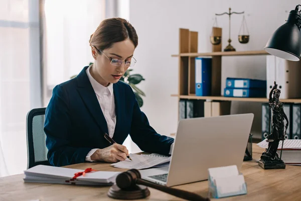 Vue latérale de avocate faisant de la paperasserie sur le lieu de travail avec ordinateur portable au bureau — Photo de stock