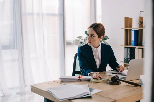 Avocate sur le lieu de travail avec marteau, billets en dollars, pot-de-vin et ordinateur portable au bureau — Photo de stock