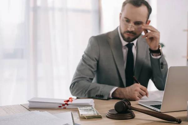 Accent sélectif de l'avocat en costume regardant l'argent sur le lieu de travail avec ordinateur portable dans le bureau — Photo de stock