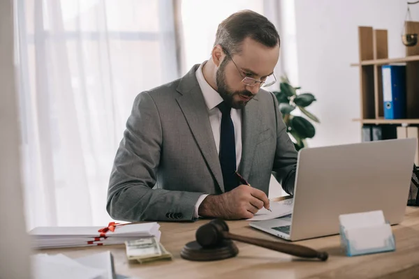 Avocat concentré en costume faire de la paperasse sur le lieu de travail avec ordinateur portable et pot de vin au bureau — Photo de stock