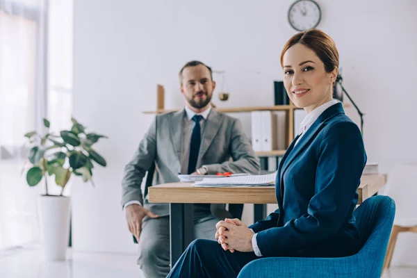 Selective focus of smiling businesswoman and colleague behind at workplace in office — Stock Photo