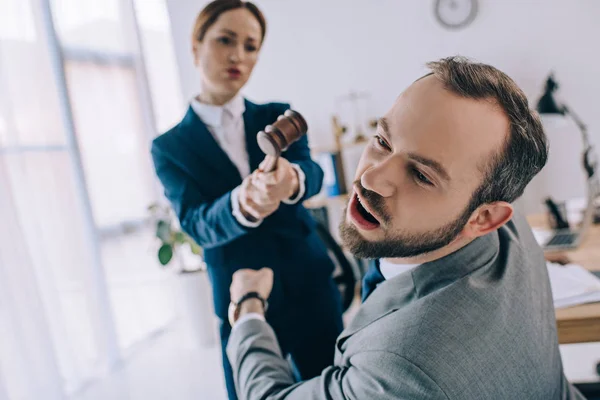 Enfoque selectivo de abogado fingiendo golpear a colega con mazo en las manos en la oficina - foto de stock