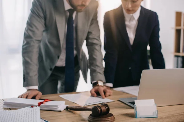 Partial view of lawyers in suits working together on project at workplace with gavel and laptop in office — Stock Photo
