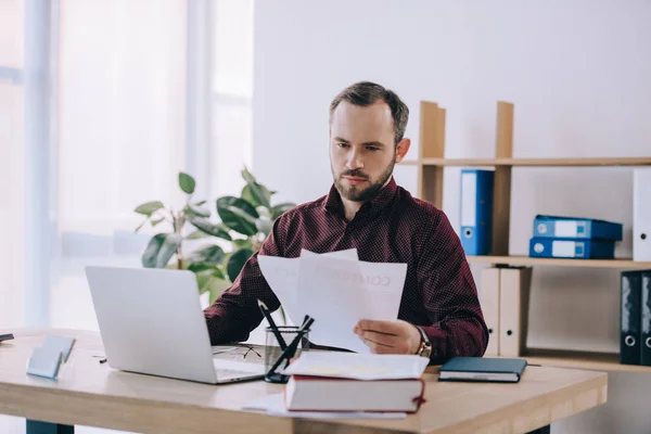 Retrato del hombre de negocios haciendo papeleo en el lugar de trabajo con el ordenador portátil en la oficina - foto de stock