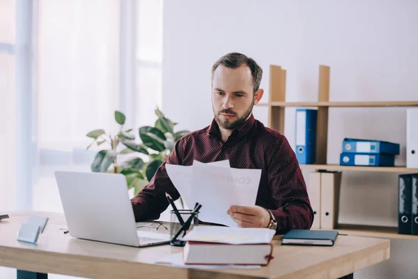 Portrait of businessman doing paperwork at workplace with laptop in office — Stock Photo