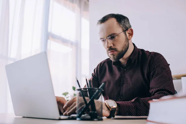 Ориентированный бизнесмен в очках, работающий на ноутбуке на рабочем месте в офисе — стоковое фото