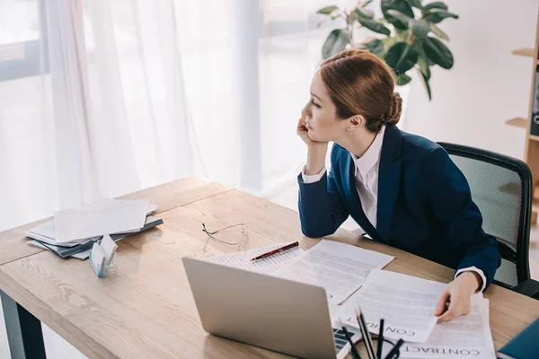 Вдумлива бізнес-леді, дивлячись далеко, сидячи на робочому місці з ноутбуком в офісі — Stock Photo
