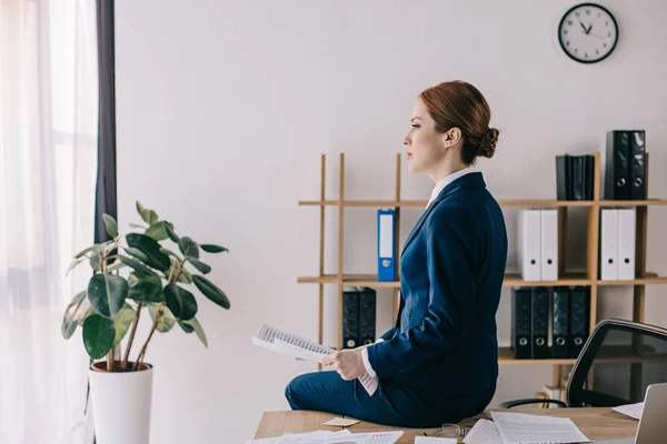 Side view of pensive businesswoman with papers sitting on table in office — Stock Photo