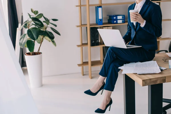 Vista parziale di donna d'affari con computer portatile e caffè per andare seduti sul tavolo in ufficio — Foto stock