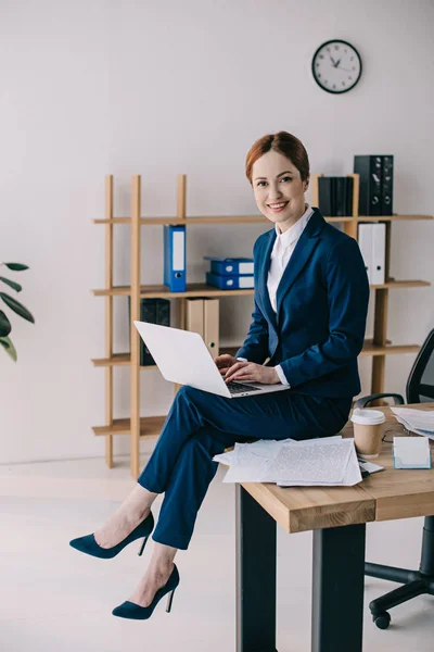 Lächelnde Geschäftsfrau mit Laptop sitzt auf Tisch im Büro — Stockfoto