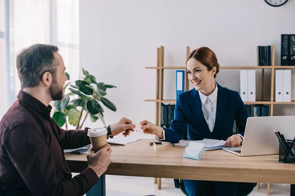 Mujer de negocios sonriente dando tarjeta en blanco al cliente con café para ir en el lugar de trabajo en la oficina — Stock Photo