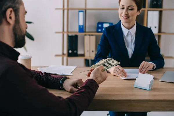 Partial view of man giving bribe to smiling businesswoman at workplace in office — Stock Photo