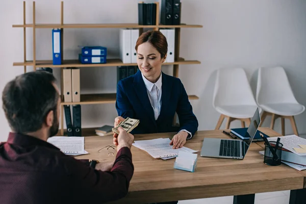 Чоловік дає хабар усміхненій бізнес-леді на робочому місці в офісі — стокове фото