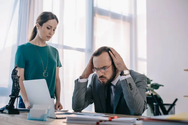 Abogado pensativo y cliente en el lugar de trabajo con computadora portátil y papeles en la oficina - foto de stock