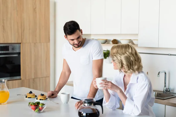 Heureux jeune couple regardant l'autre tout en prenant le petit déjeuner ensemble — Photo de stock