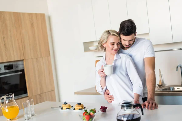 Glückliches junges Paar umarmt sich beim Frühstück in der Küche — Stockfoto