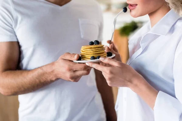 Foto recortada de pareja joven sosteniendo deliciosos panqueques con arándanos - foto de stock