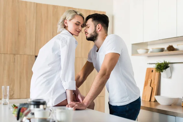 Vista lateral de feliz casal jovem sensual com olhos fechados tocando as testas na cozinha — Stock Photo
