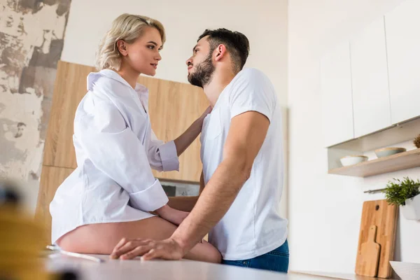 Vista lateral de sensual pareja joven mirándose en la cocina por la mañana - foto de stock