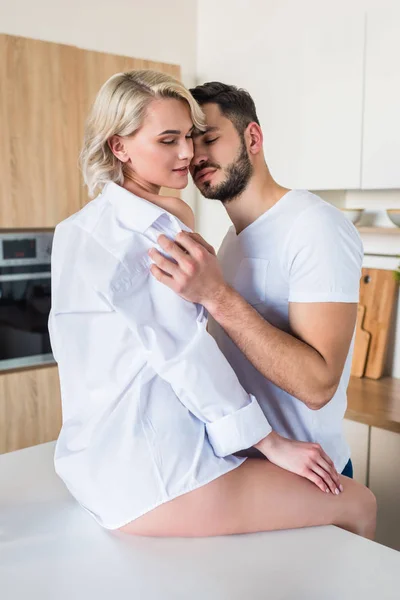 Seductora pareja joven feliz abrazándose en la cocina por la mañana - foto de stock