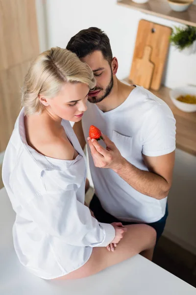 Высокий угол зрения соблазнительной молодой пары едят клубнику на кухне — стоковое фото
