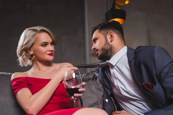 Seductora joven pareja bebiendo vino, mujer sosteniendo corbata de guapo novio - foto de stock