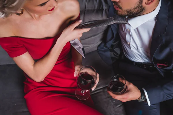 Recortado tiro de moda pareja bebiendo vino, mujer sosteniendo corbata de guapo novio - foto de stock