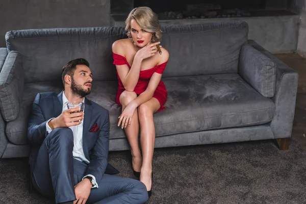 Bell'uomo in tuta che tiene un bicchiere di whisky e guarda la ragazza sexy con il sigaro — Foto stock