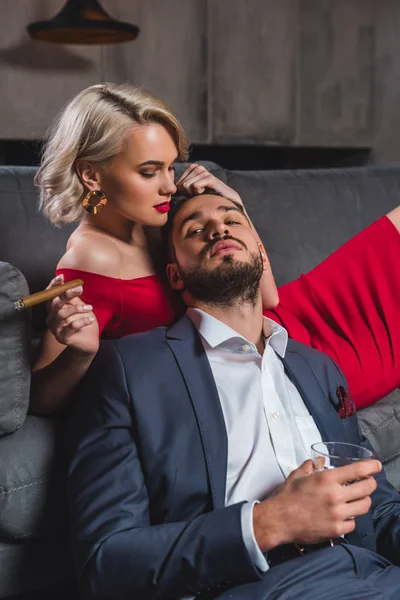 Seductive young woman holding cigar and touching handsome man with glass of whisky — Stock Photo
