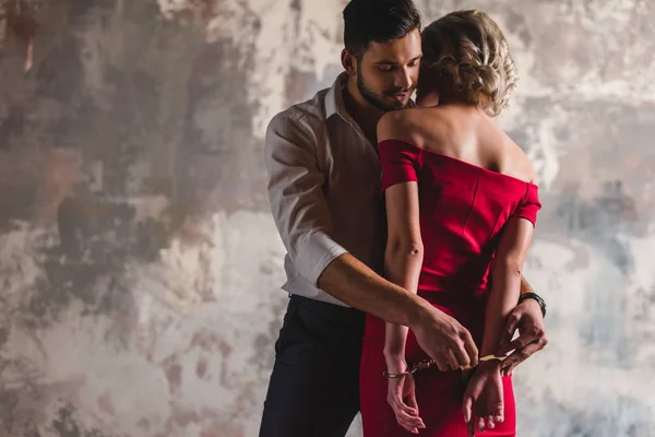 Joven guapo poniendo esposas en mujer seductora en vestido rojo - foto de stock