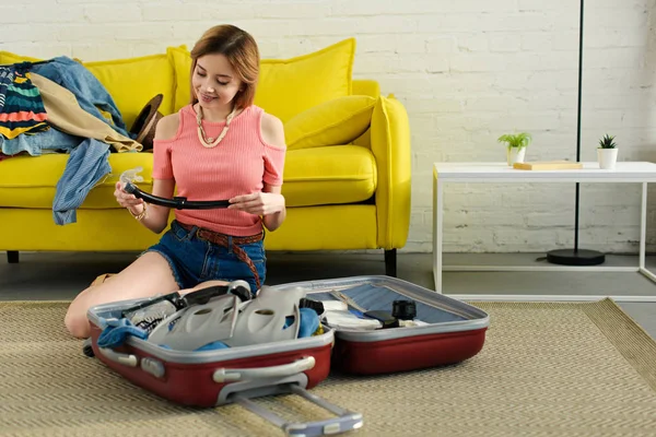 Smiling girl packing snorkeling mask and fins into suitcase for travel — Stock Photo