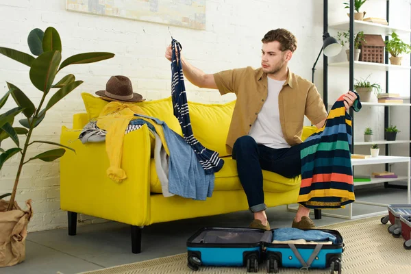 Hombre guapo embalaje ropa en bolsa de viaje - foto de stock