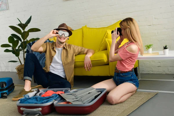 Young girl taking photo of boyfriend in goggles while preparing for a vacation — Stock Photo
