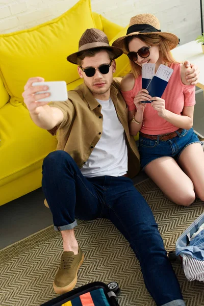 Пара в солнечных очках с паспортами и авиабилетами, делающими селфи на смартфоне — стоковое фото