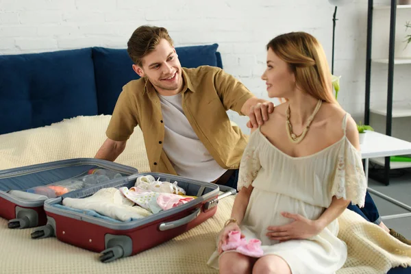 Беременная жена и счастливый муж собирают чемодан для больницы дома — стоковое фото