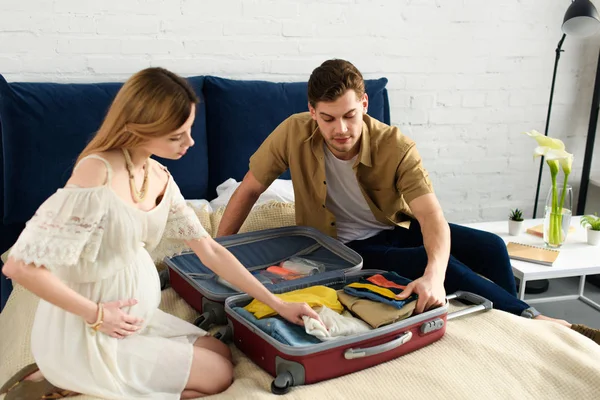 Mujer embarazada y marido embalaje bolsa de viaje para vacaciones - foto de stock