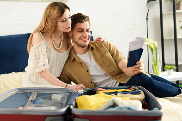 Young happy couple packing suitcase and holding passports with air tickets — Stock Photo