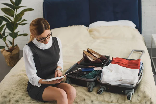 Mujer de negocios leyendo diario mientras que hace las maletas para el viaje de negocios - foto de stock