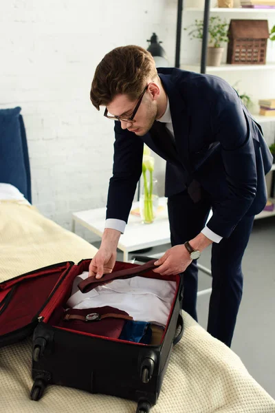 Молодой привлекательный бизнесмен в костюме упаковывает чемодан для деловой поездки — стоковое фото