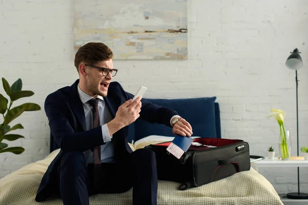 Late businessman yelling while looking at smartphone and holding passport with ticket for business trip — Stock Photo