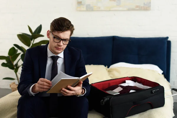 Bel homme d'affaires en costume lecture journal tout en se préparant pour le voyage d'affaires — Photo de stock