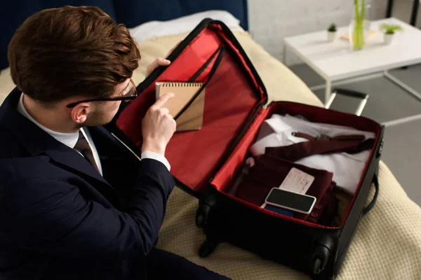 Bel homme d'affaires emballage journal, smartphone et vêtements dans un sac de voyage — Photo de stock