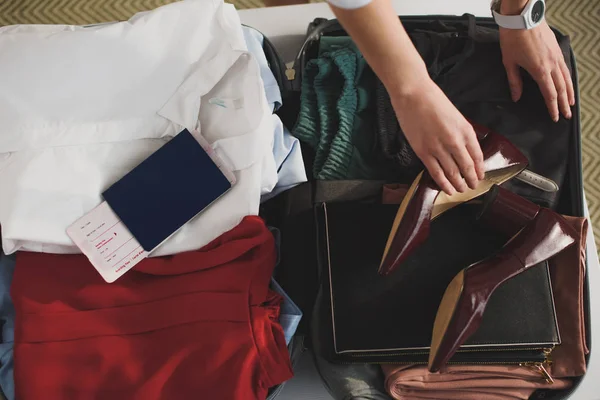 Обрізаний вид жінки, що упаковує одяг та паспорт у валізі — стокове фото