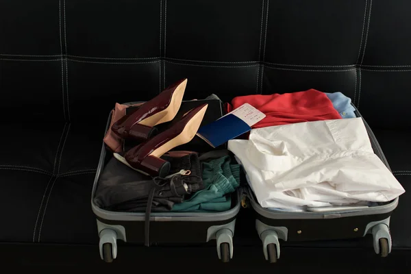 Opened travel bag with passport, clothes and heels on sofa — Stock Photo