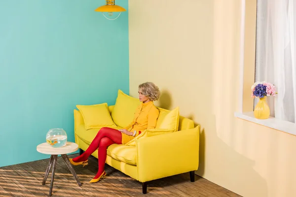 Mujer en ropa retro brillante descansando en el sofá en el apartamento colorido, concepto de casa de muñecas - foto de stock